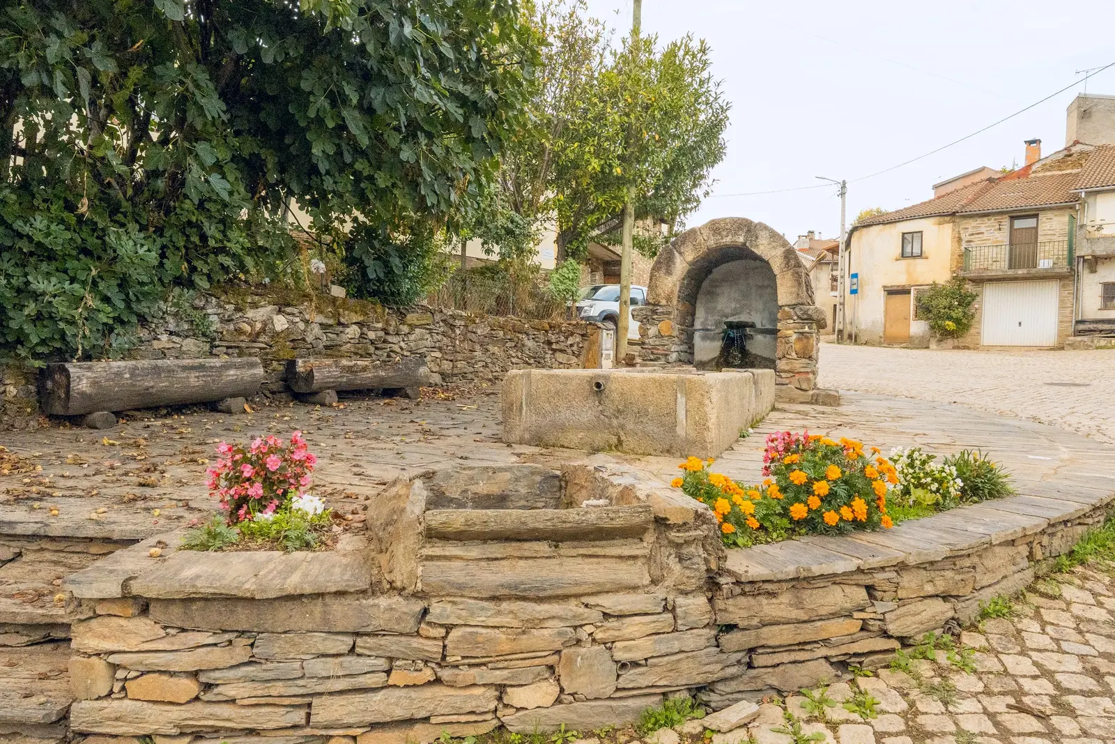 Fonte e lavadouro de pedra, com canteiros de flores, no centro da aldeia