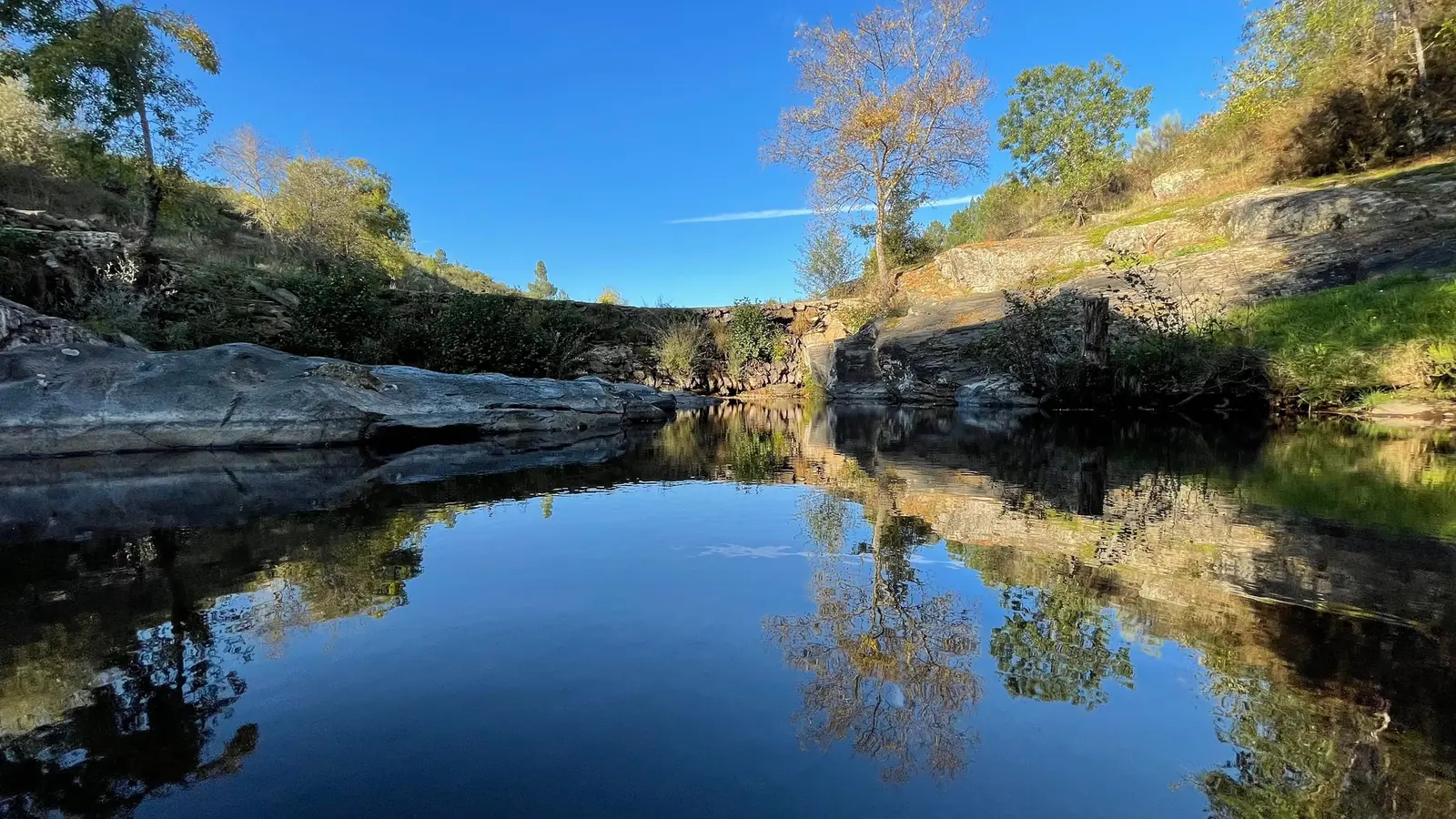Poça de água calma no rio, entre rochas e árvores