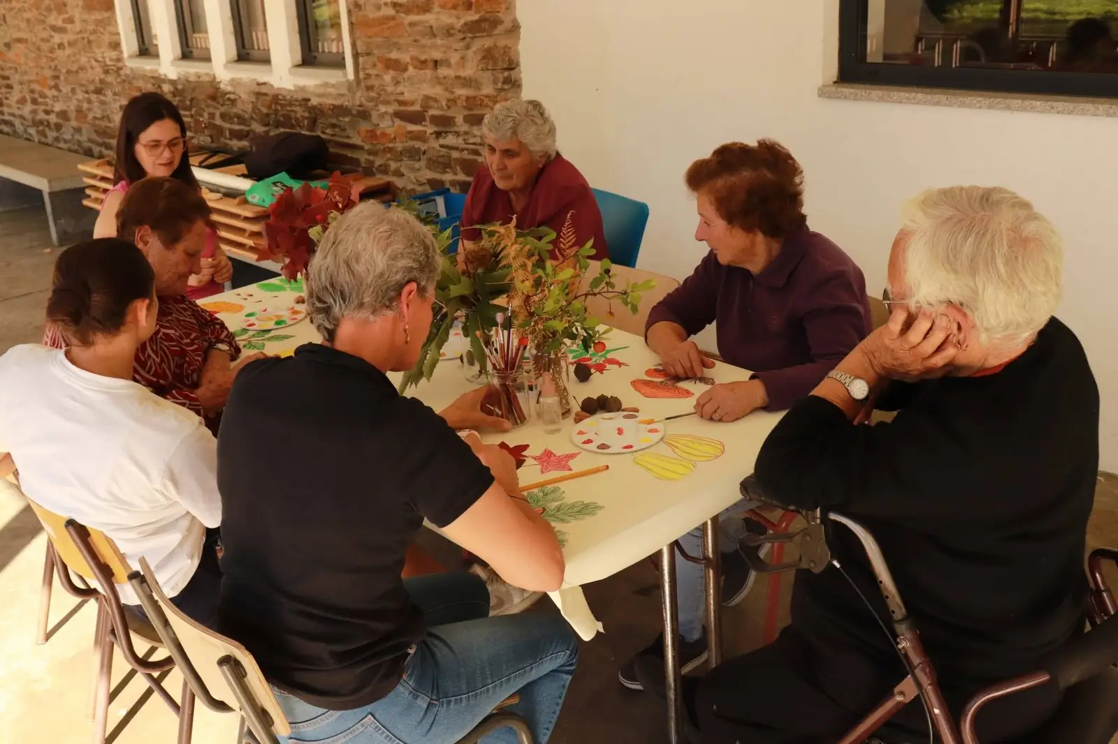 Participantes na oficina de desenho e pintura, sentadas à volta de uma mesa com ramos de folhas de Outono, tintas e pincéis