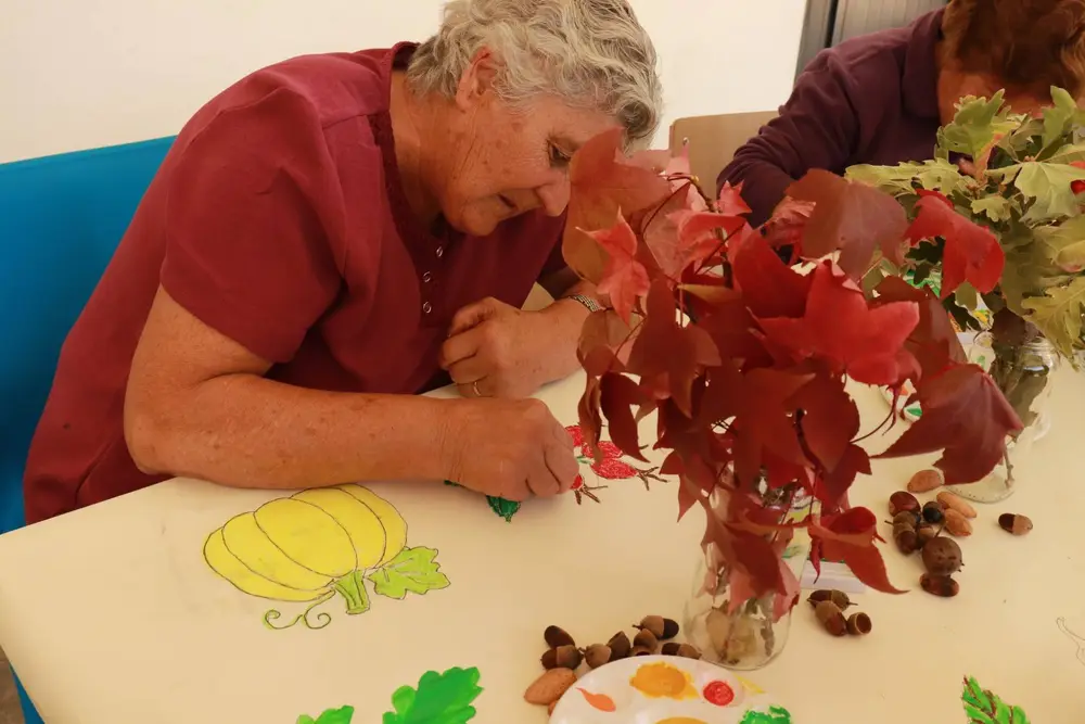 Participante a colorir uma abóbora amarela e rosa-canina, ao lado de um ramo de folhas vermelhas de Outono e de bolotas