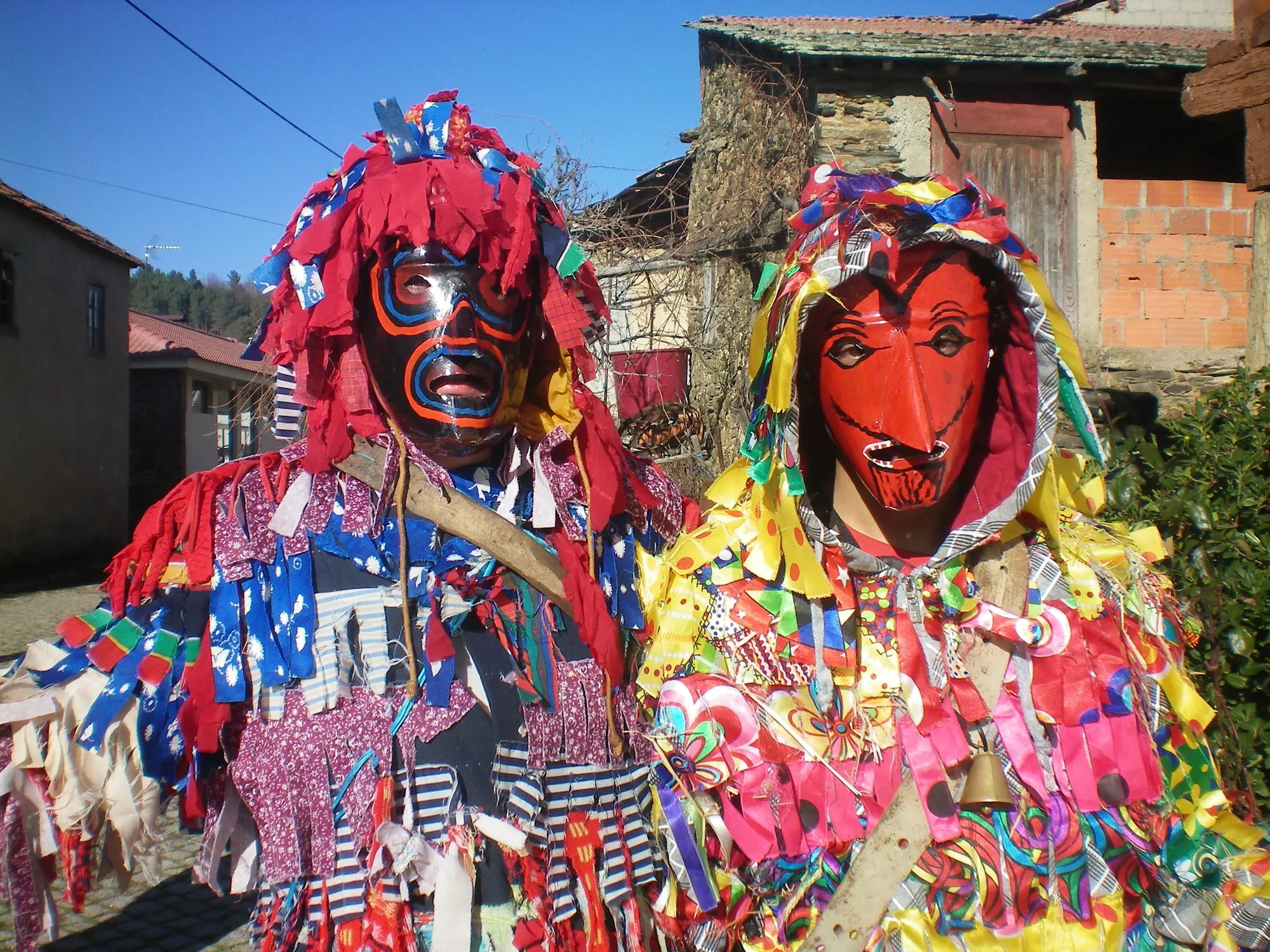 Dois caretos de máscaras vermelhas e fatos de retalhos de muitas cores
