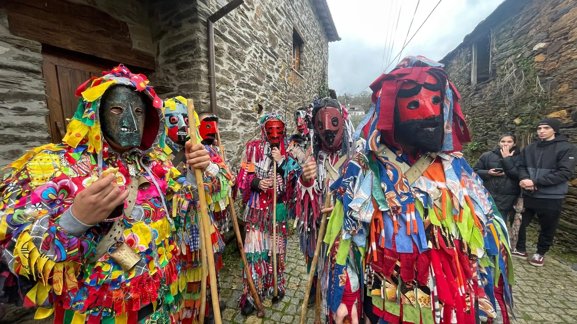 Grupo de caretos de fatos de retalhos coloridos e máscaras de lata, numa rua de pedra de Varge